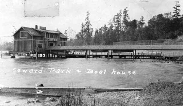 black and white photo of wooden building on pier and connected by long covered boardwalk